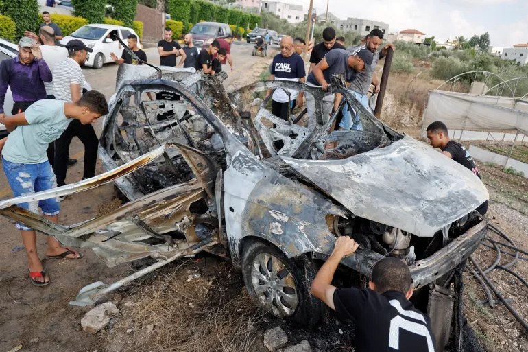 Palestinians inspect a vehicle damaged in an Israeli air attack near Tulkarem [Raneen Sawafta/Reuters]